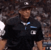a baseball referee wearing a mlb hat stands in front of a crowd