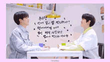 two young men are sitting at a table with korean writing on it