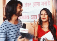 a man and a woman are talking to each other in front of a sign that says ' aar aana mana '