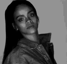 a black and white photo of a woman wearing a denim jacket looking at the camera .