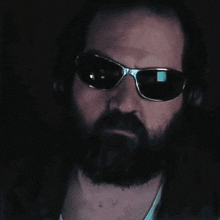 a man with a beard wearing sunglasses and headphones is pointing his finger at the camera .
