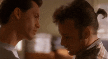 a man with a ponytail is looking at another man 's face .