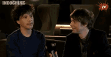 two men are sitting next to each other smiling and the word indochine is on the bottom right