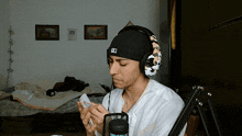 a man wearing headphones and a hat with the letter d on it looks at his phone