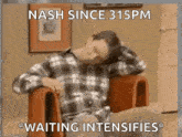 a man in a plaid shirt is sitting in a chair with his hand on his head .
