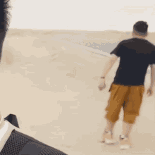 a man in a black shirt and yellow shorts walks on a sandy beach