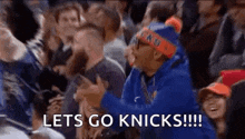 a man in a blue hoodie is sitting in a crowd of people watching a basketball game and screaming .