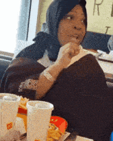 a woman wearing a hijab is sitting at a table with a mcdonald 's cup in front of her