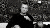 a black and white photo of a man holding a cigarette in front of a rug