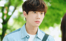 a young man wearing a denim jacket and a white shirt is looking at someone
