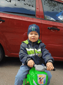 a young boy is sitting on a green toy motorcycle with the word racer on the front