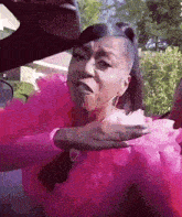 a woman in a pink dress is sitting in a car with her hand on her chest .