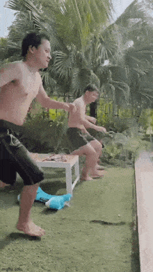 two men are jumping into a swimming pool while another man sits on a table .