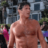 a shirtless man stands in front of a building on the beach