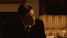 a man in a suit and tie is sitting on a couch and saying but your enemies closer .