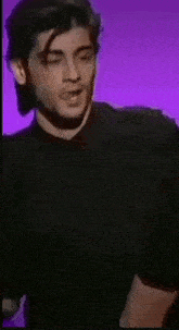 a man with a tattoo on his arm is standing in front of a purple wall