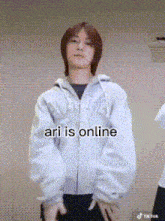 a man in a white jacket is standing in front of a wall with his hands on his hips and the caption ari is online .