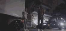 two men are standing next to each other in front of a building and a car .