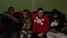 a group of people are sitting on a couch with one wearing a red sweater with a teddy bear on it