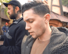 a man with a beard is standing next to another man wearing a black hat