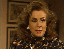 a woman wearing a black dress and a necklace is looking at the camera