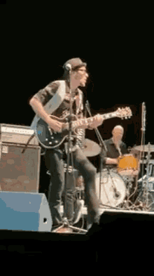 a man is playing a guitar on a stage while a drummer plays drums .