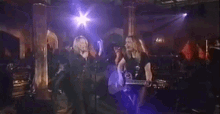 a woman is playing a guitar while another woman sings into a microphone on stage .