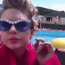 a woman wearing sunglasses and a red coat is standing in front of a swimming pool
