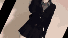 a woman wearing a black cardigan and a black skirt is standing in front of a wall .