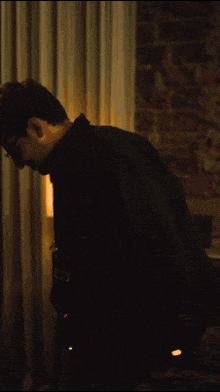a man in a black jacket and glasses is standing in a dark room