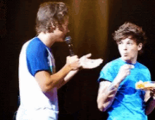 a man in a blue shirt is talking into a microphone while another man looks on