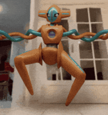 a toy robot with blue arms and legs is flying in front of a window