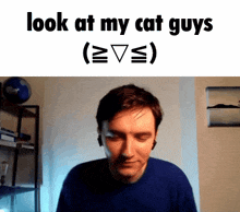 a man in a blue shirt is looking at the camera with the caption " look at my cat guys "