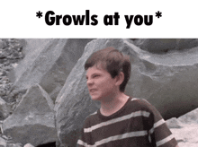 a boy in a striped shirt is standing in front of rocks with the words " growls at you " above him