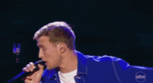 a man in a blue jacket is singing into a microphone with abc written on his jacket