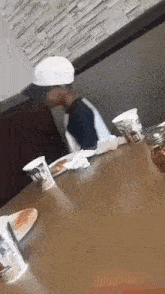 a man in a white hat is sitting at a table with a plate of food and cups .