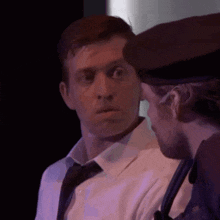a man in a white shirt and tie is standing next to another man in a hat .