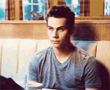 a man in a grey shirt is sitting at a table with a cup of coffee and a glass of water .