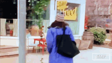 a woman in a blue coat is walking down a street in front of a store that sells food