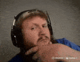 a man with a beard wearing headphones and a blue shirt is looking at the camera .
