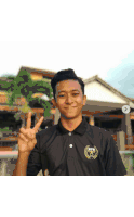 a young man wearing a black shirt with a gold emblem on it giving the peace sign