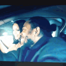 a man with a ponytail is driving a car with a woman in the back seat