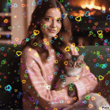 a woman is holding a kitten in her arms and hearts are flying around her