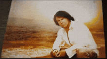 a man in a white shirt sits on the beach looking at the ocean