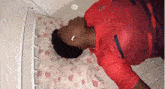 a man in a red shirt is sleeping on a bed with a pillow .