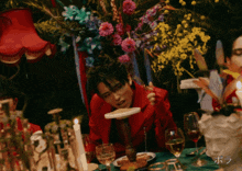a man in a red jacket sits at a table with candles and flowers
