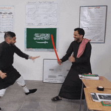two men are fighting in front of a green flag with arabic writing on it
