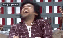 a man in a plaid shirt is sitting on a couch laughing .
