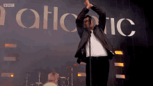 a man sings into a microphone in front of a sign that says bbc