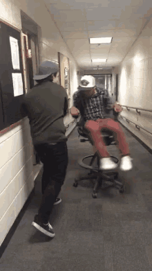 two men are dancing in a hallway with one wearing a white hat